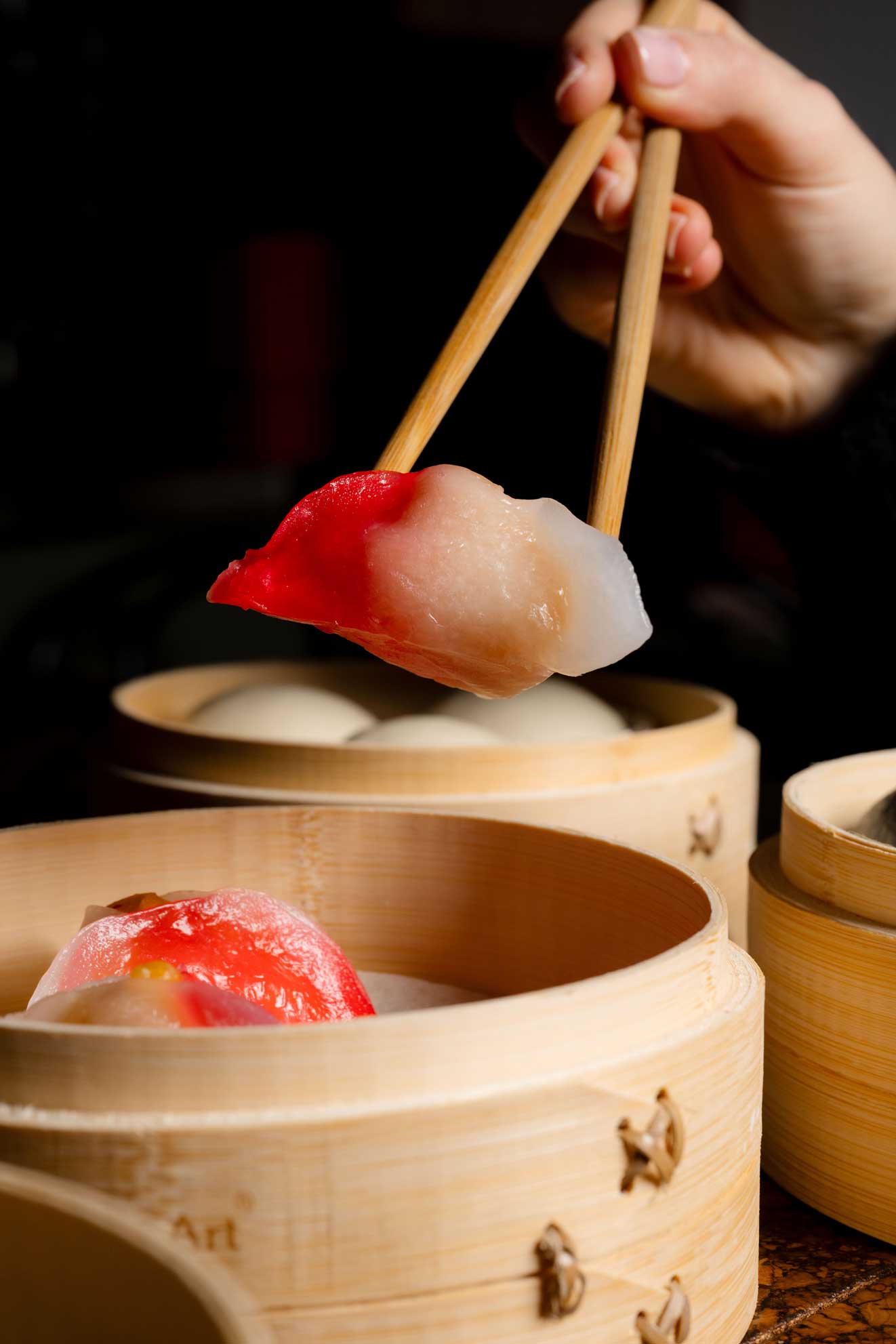 Close-up of a translucent dumpling being lifted with chopsticks from a bamboo steamer.