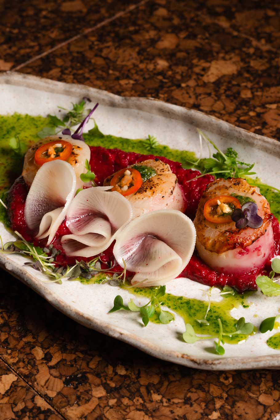 Beautifully plated scallops on beetroot purée, garnished with sliced radish and microgreens.