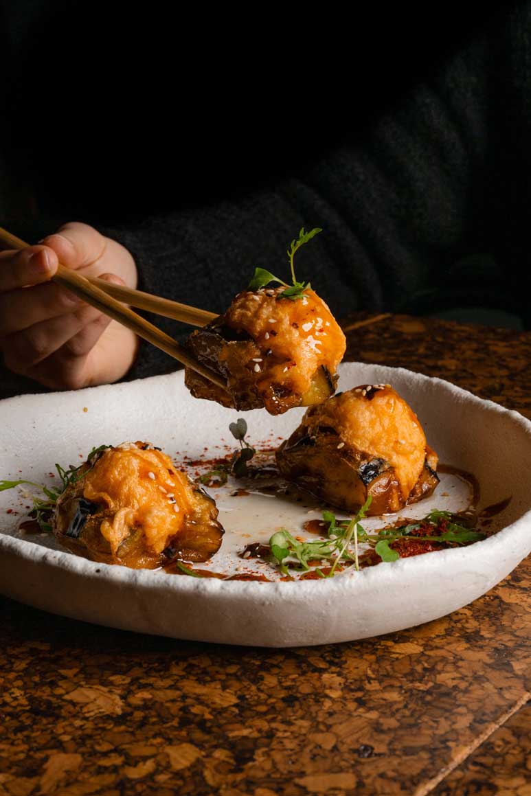 Chopsticks lifting a crispy golden dumpling from a rustic white bowl, garnished with microgreens