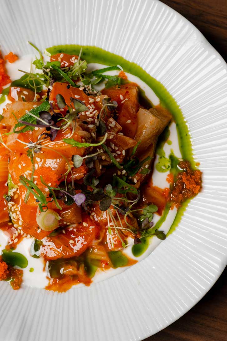 Fresh salmon sashimi salad with sesame, scallions, and microgreens on a white plate.